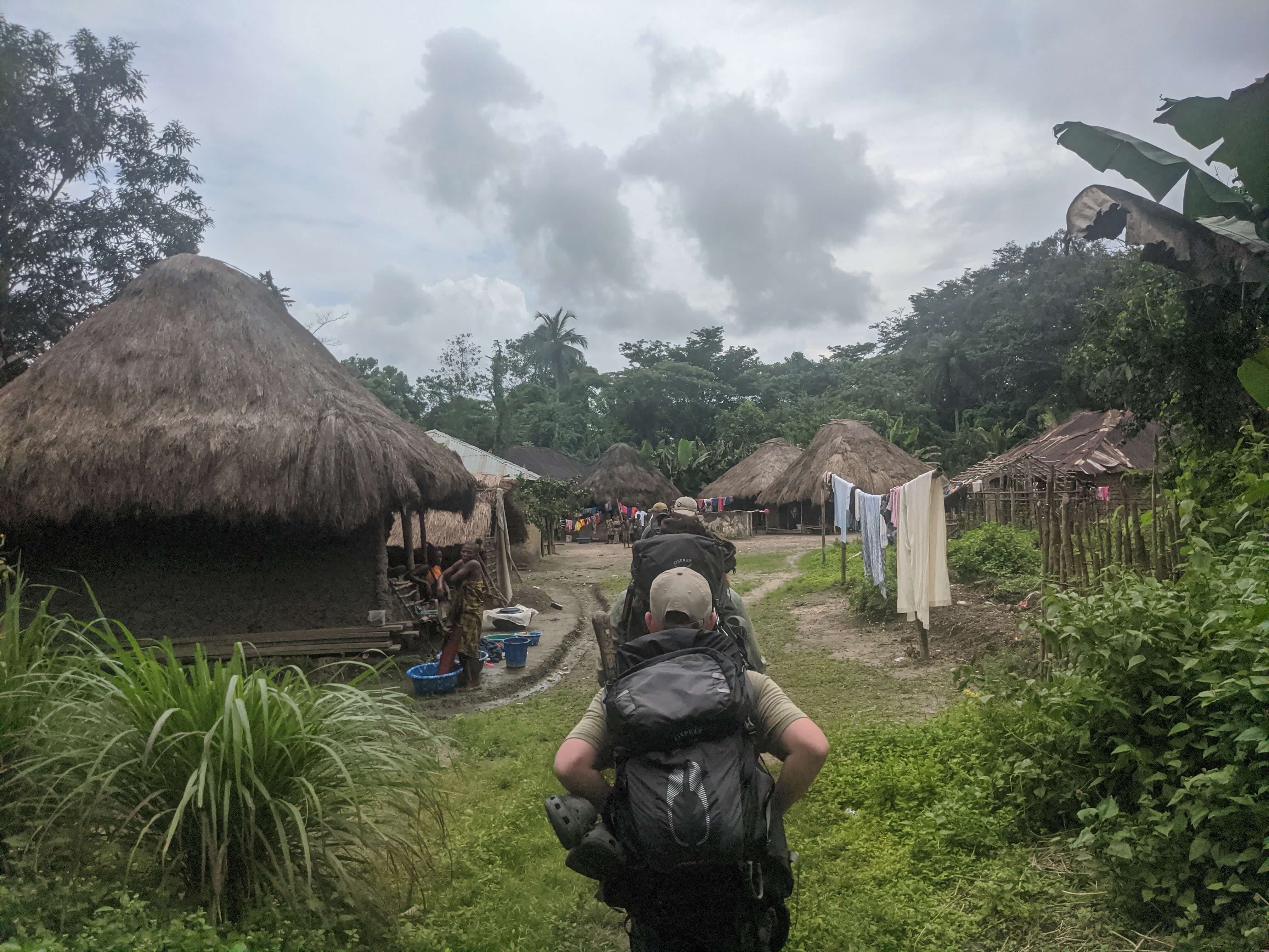 Line of men with backpacks walking into a remote village.